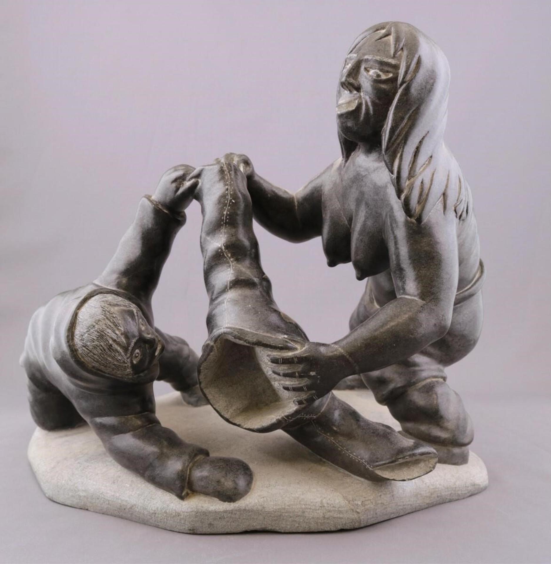 Levi Alashuak (1951) - a grey stone carving of a Man and Woman with a Pair of Trousers