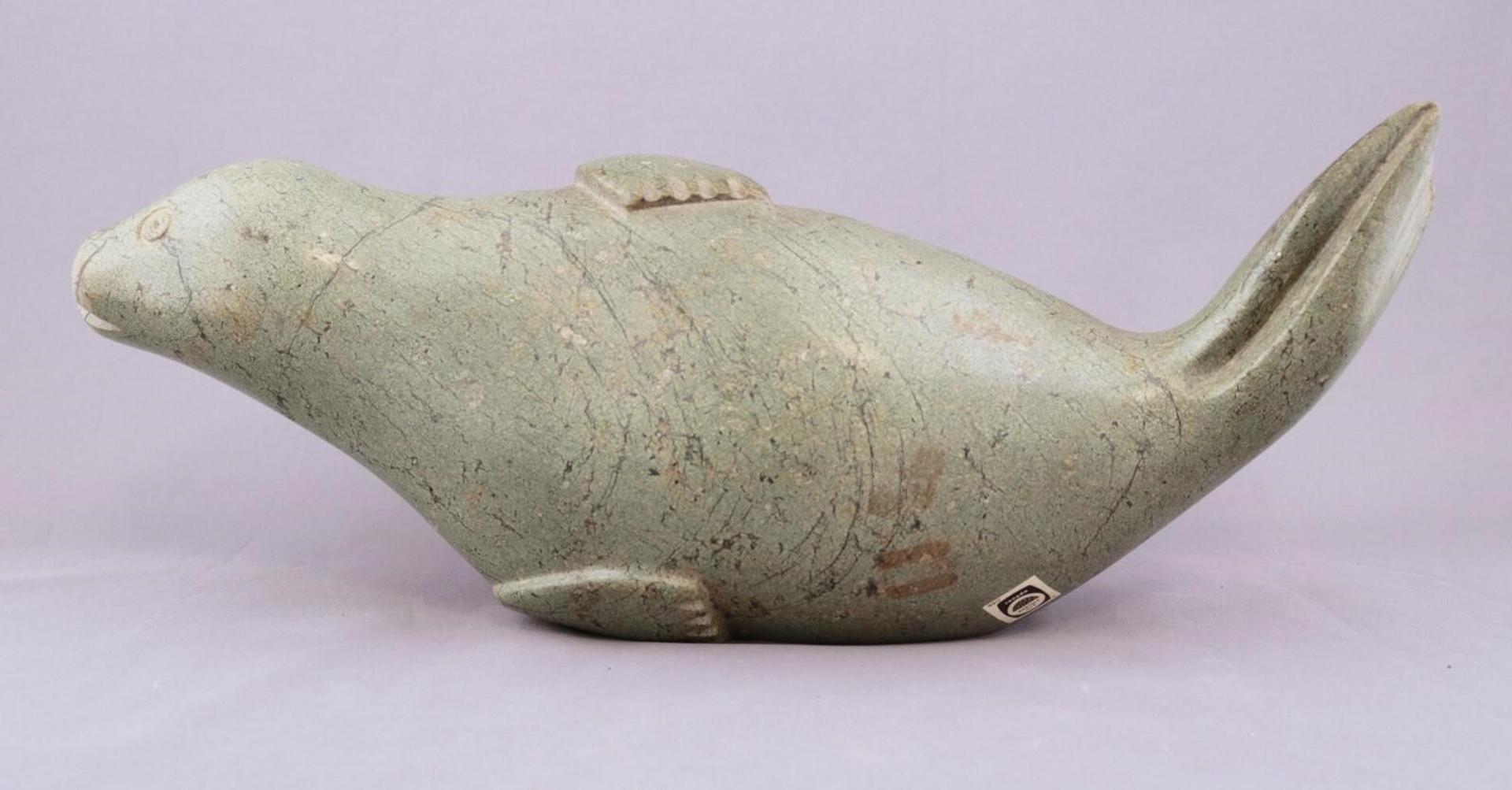 Nikotai Simigak (1947) - a green-tan stone carving of a Seal Lying on its Side